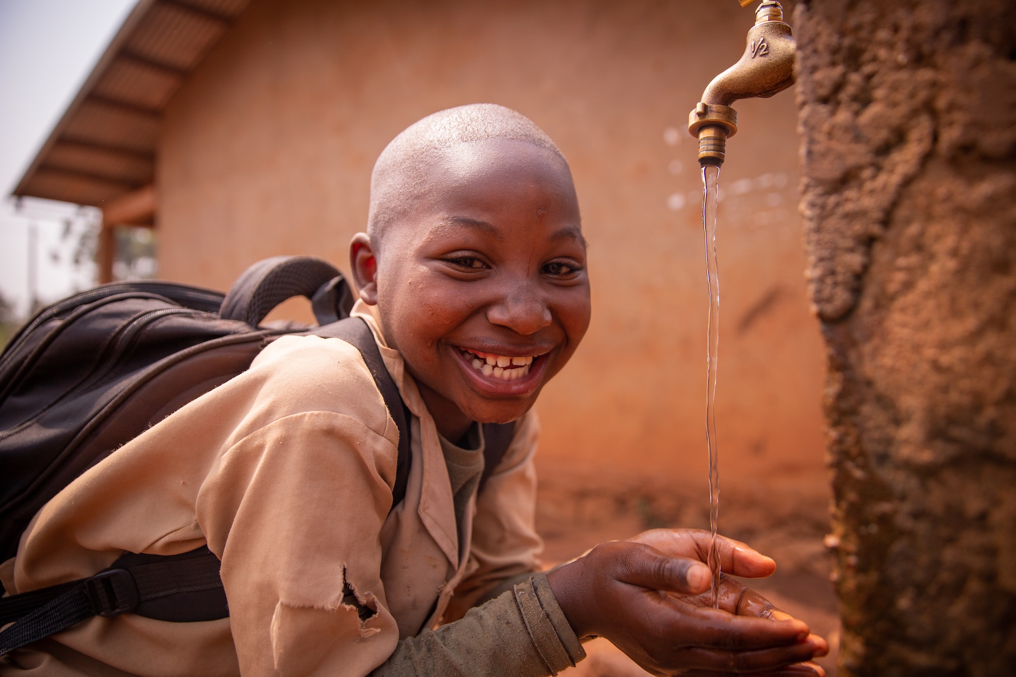African schoolboy at school smiles drinking water from the tap outside in the courtyard